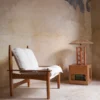 Butaca de madera con cojines blancos en una sala con luz natural de La Maison Barcelona, perfecta para una decoración hogareña