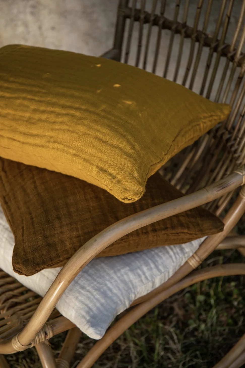Cojín de lino color mostaza en una silla de madera, sobre un fondo natural.