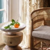 Mesa auxiliar con decoración de frutas junto a una silla de mimbre