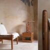 Butaca de madera con cojines blancos junto a una mesa de madera en un ambiente rústico de La Maison Barcelona, perfecta para una decoración completa