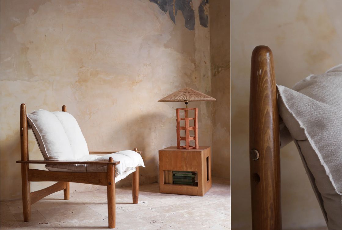 Butaca de madera con cojines blancos junto a una mesa de madera en un ambiente rústico de La Maison Barcelona, perfecta para una decoración completa
