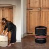 Mujer colocando una cesta con tapa en color blanco crema frente a una puerta de madera, junto a una cesta negra con rayas rojas