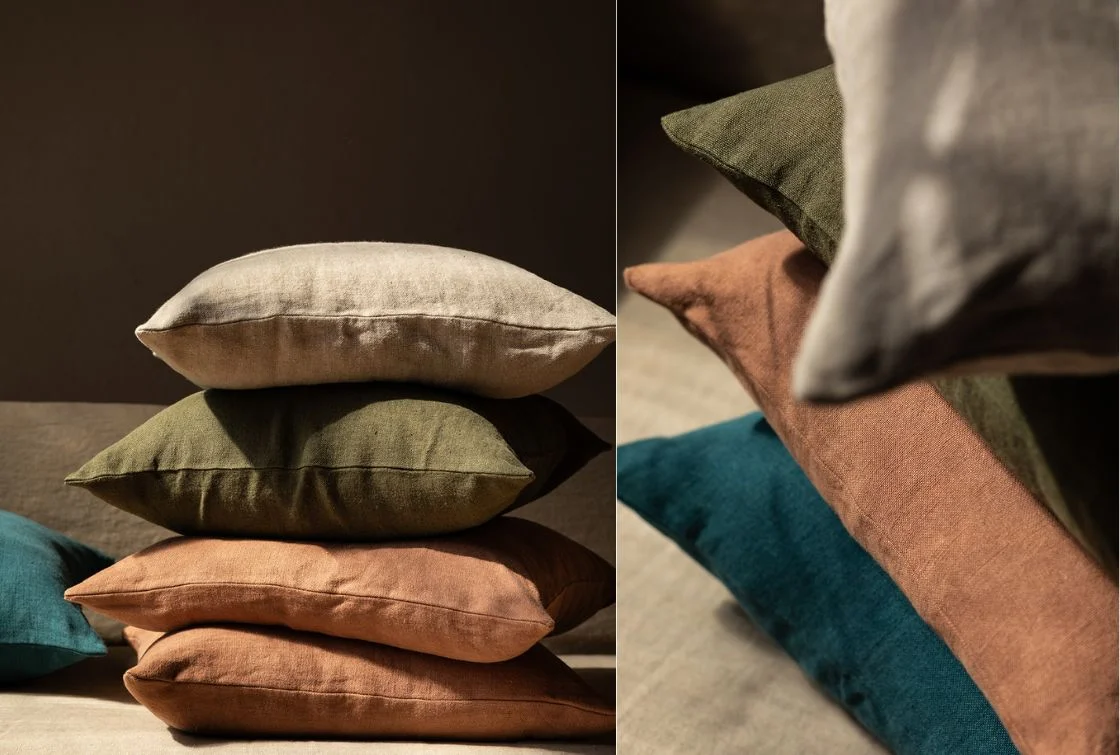 Pila de cojines de lino en varios colores: verde, beige, azul y terracota, sobre un fondo oscuro.