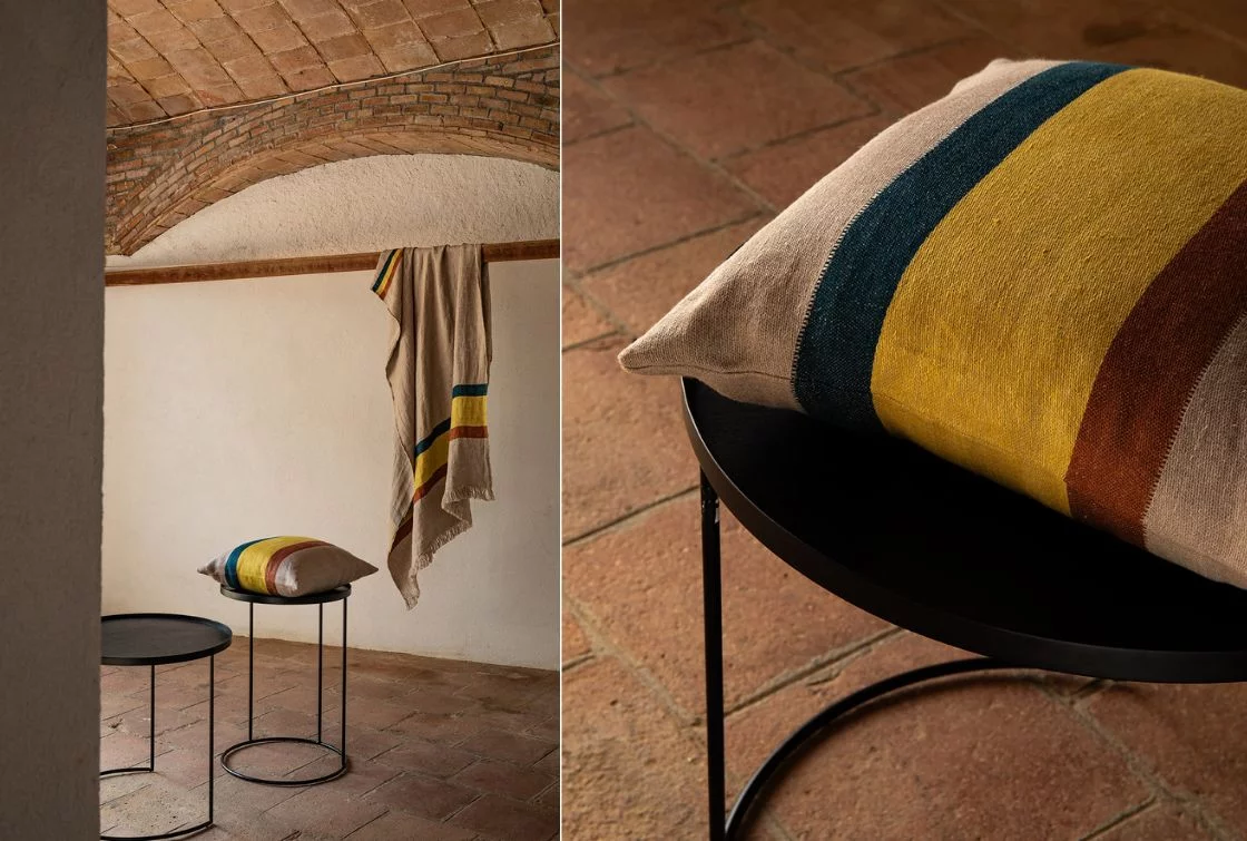 Cojín de lino con rayas en colores tierra y azul sobre una cama con cabecera de madera con tapizado floral.