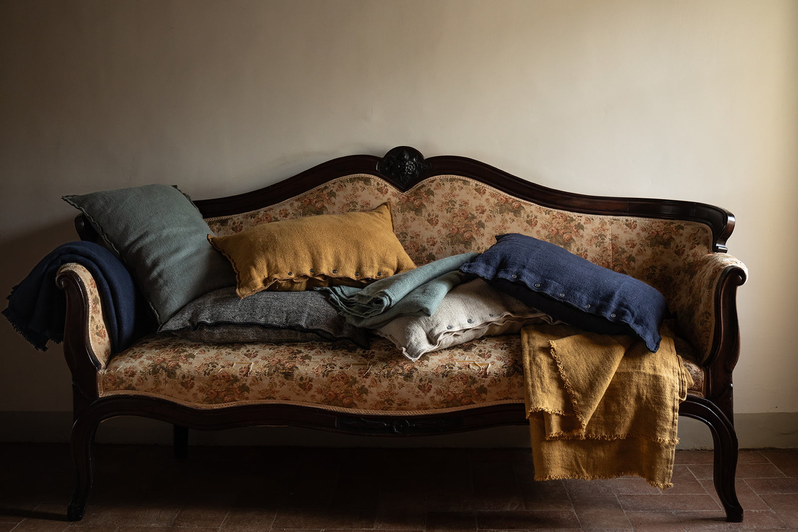 Sofá antiguo con cojines decorativos y manta de lana amarilla.