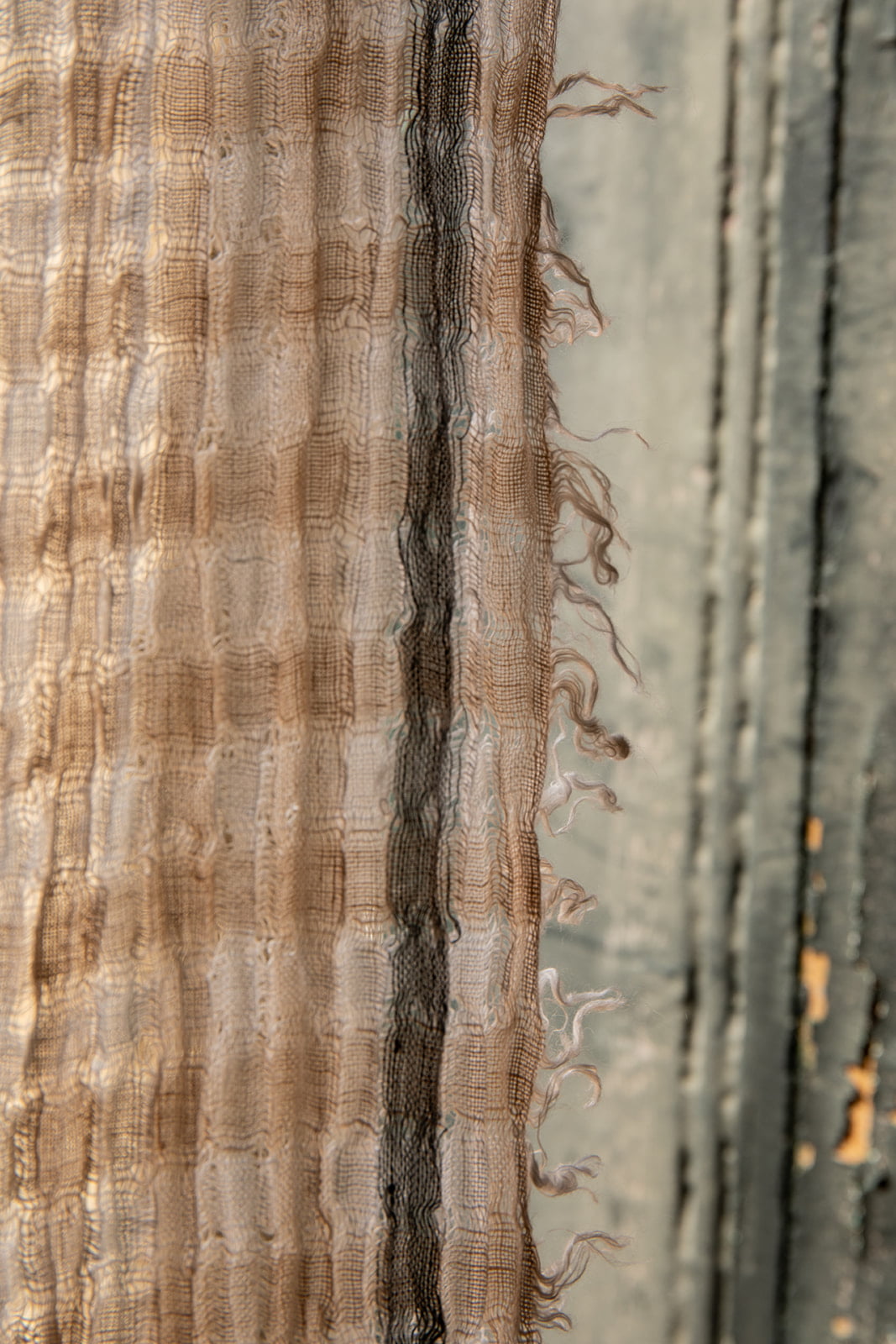 Primer plano de una tela de lino en tonos beige y marrón colgada en una pared de textura rústica