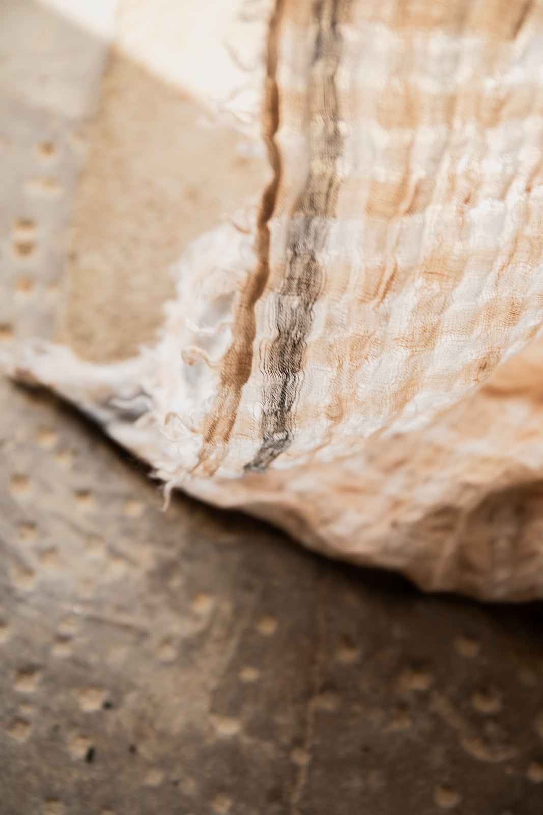 Primer plano de una tela de lino en tonos beige y marrón colgada en una pared de textura rústica