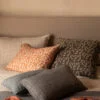 Cojines de lino en tonos grises, beige y naranjas a rayas sobre una cama de lino con cabecera de madera.