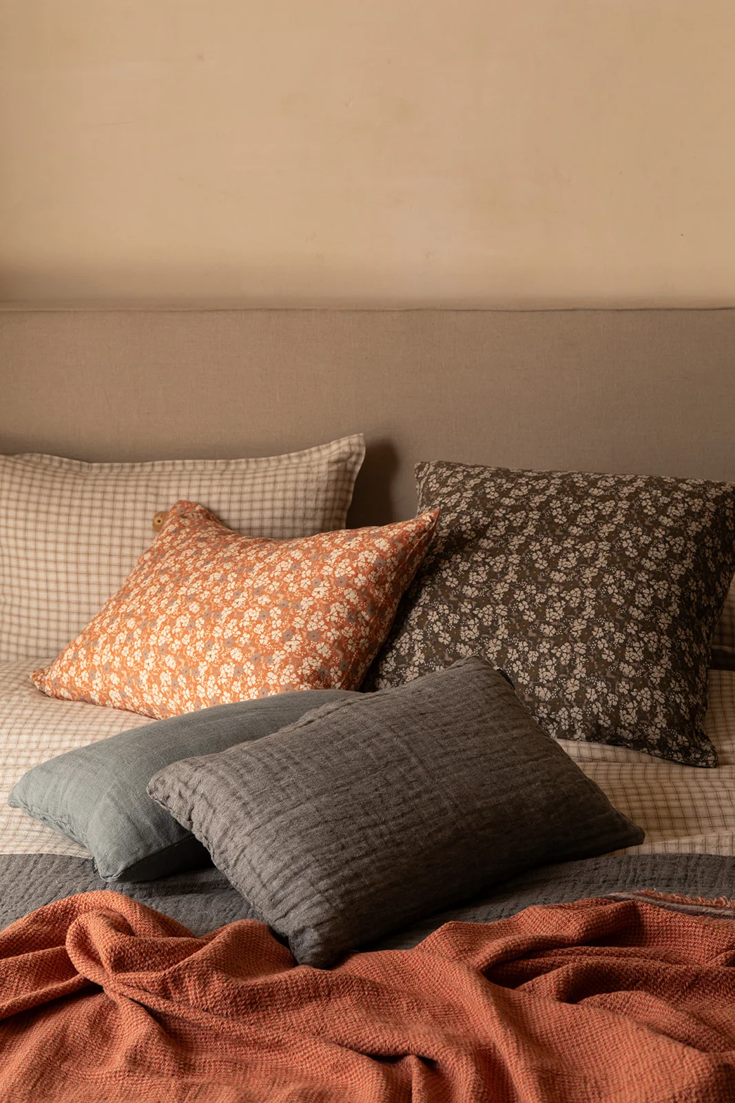 Cojines de lino en tonos grises, beige y naranjas a rayas sobre una cama de lino con cabecera de madera.
