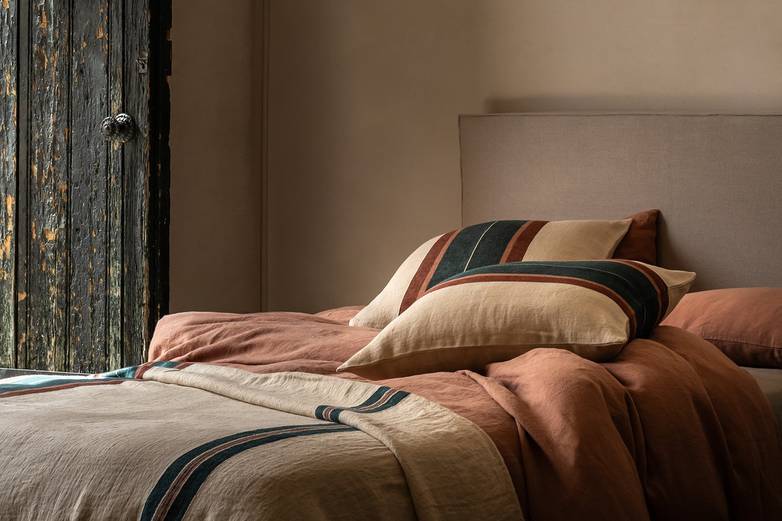 Cojines de lino con rayas multicolores sobre una cama en un ambiente rústico.