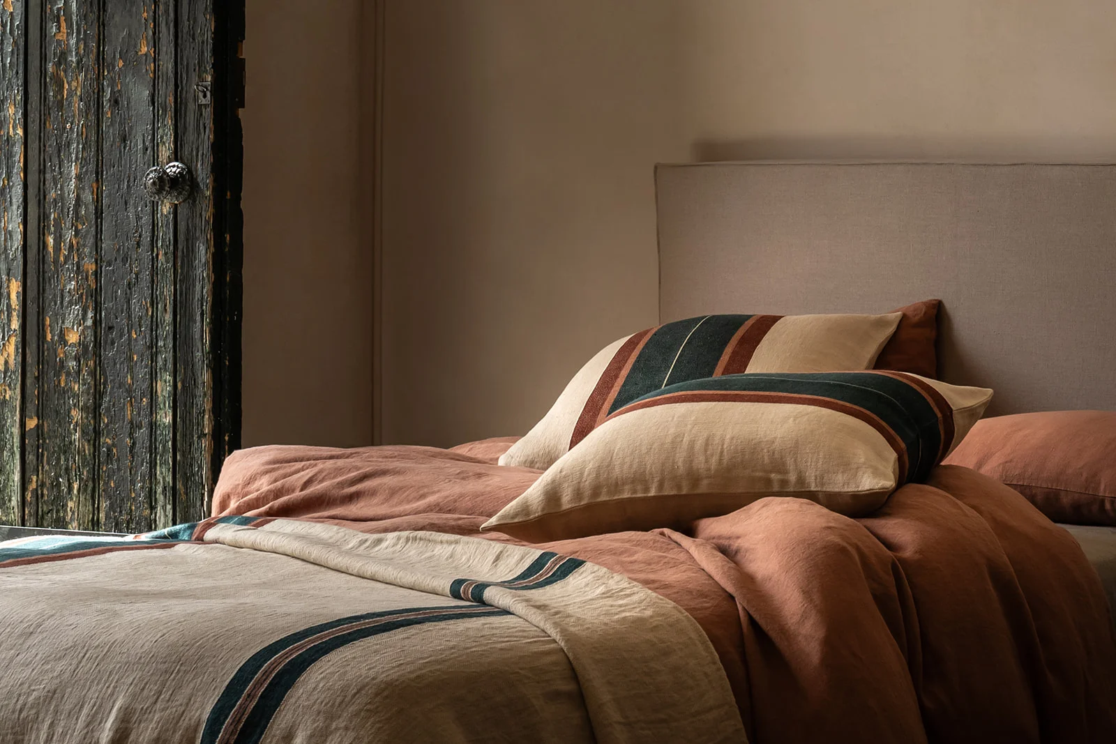 Cojines de lino con rayas multicolores sobre una cama en un ambiente rústico.