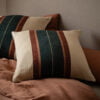 La Maison Barcelona 2024 Cojines de lino con rayas multicolores sobre una cama en un ambiente rústico.