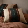 Cojines de lino con rayas multicolores sobre una cama en un ambiente rústico.