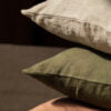 Almohadas de lino en tonos verdes, grises y marrones apiladas.
