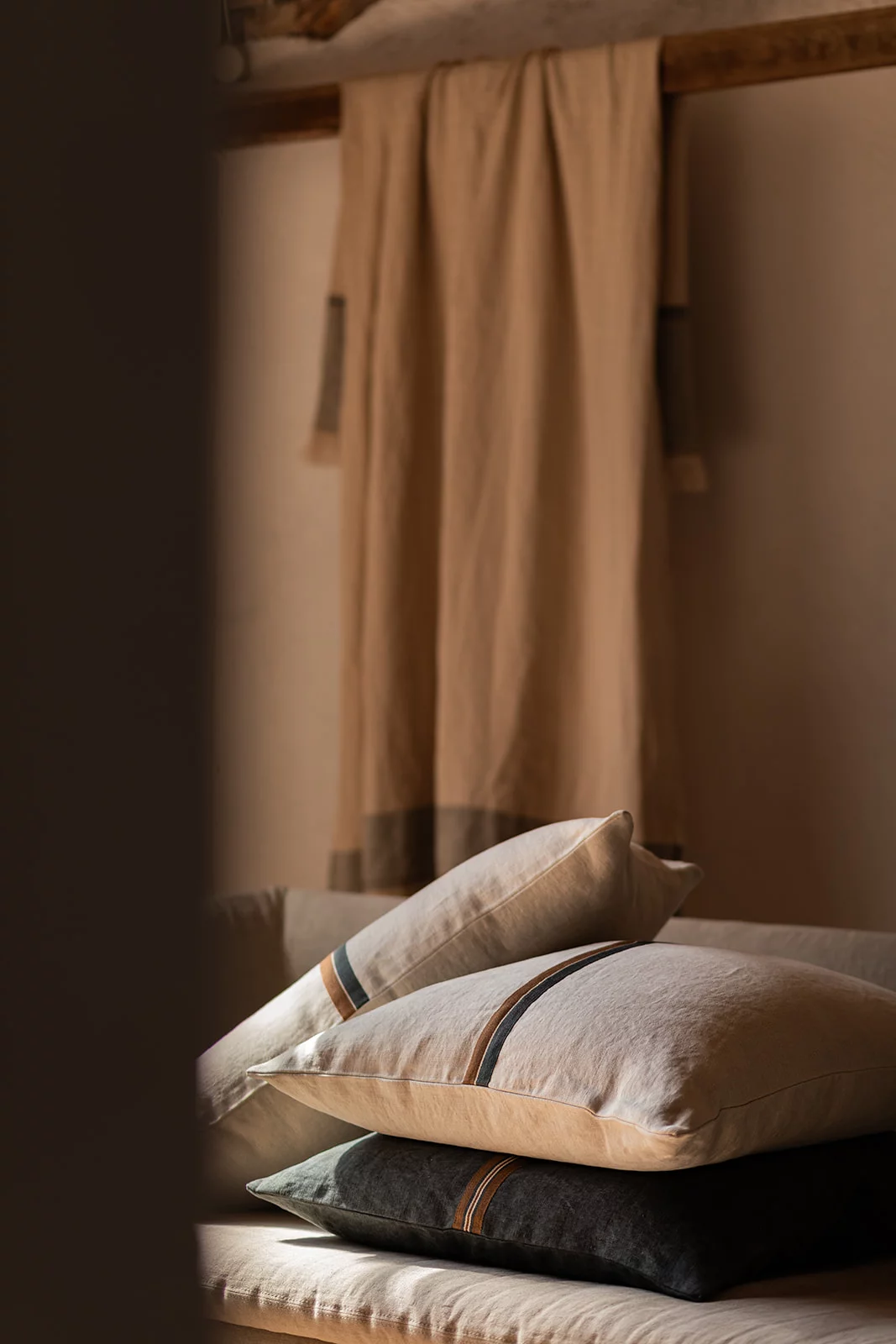 Cojines de lino apilados en tonos beige y gris en un ambiente cálido.