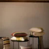 Cojín de lino con rayas en colores tierra y azul sobre una mesa redonda de metal negro con fondo de pared blanca.