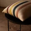 Cojín de lino con rayas en colores tierra y azul sobre una mesa redonda de metal negro.