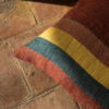 Cojín de lino con franjas de colores: amarillo, verde, azul y rojo, sobre suelo de baldosas.