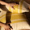 La Maison Barcelona 2024 Cojines de lino en tonos amarillos y blancos a rayas sobre una cama de lino con cabecera de madera.