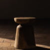 Taburete de madera con diseño cilíndrico en una habitación con piso de ladrillo y luz natural