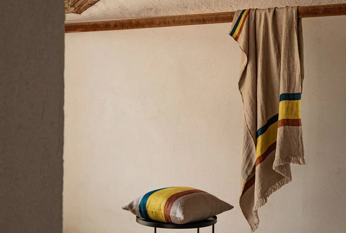 Manta a rayas y cojines sobre sillas negras en ambiente rústico.